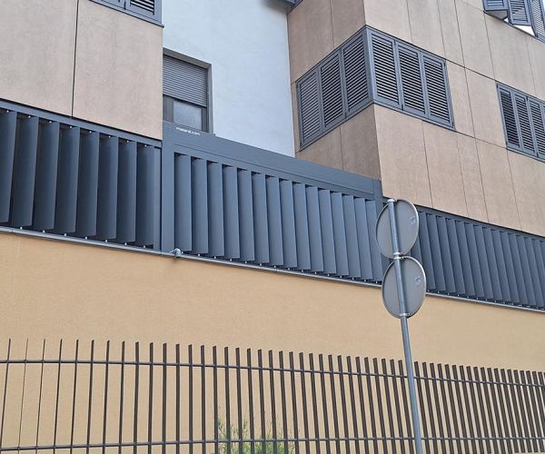 Vertikalni brisoleji Misteral v temno sivi barvi, nameščeni ob balkonu sodobne stavbe za učinkovito senčenje in zasebnost.