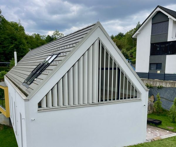 Beli trikotni brisoleji podjetja Misteral na fasadi sodobne enodružinske hiše, nameščeni pod poševno streho za zaščito pred soncem.